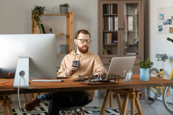 オフィスの木のテーブルに座って コーヒーを飲みながらコンピュータを使用して眼鏡で集中設計フリーランサー — ストック写真