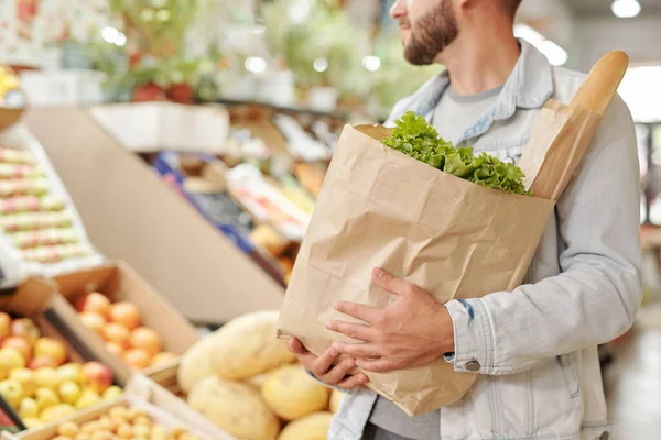 食品市場で新鮮な製品の完全な紙袋を運ぶデニムジャケットの髭男のクローズアップ — ストック写真
