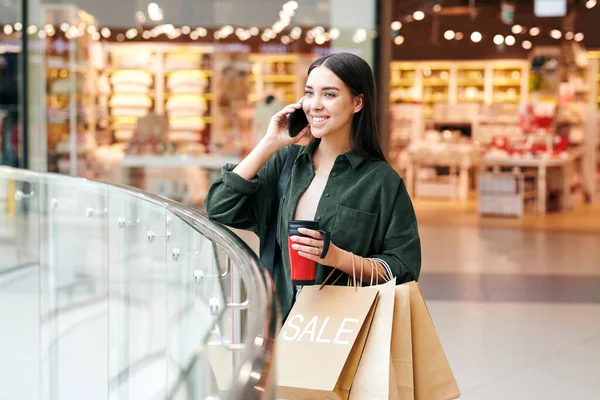 在参观了现代大型购物中心的各个部门后 年轻的成功女性顾客 带着饮料和平装本在手机上聊天 — 图库照片