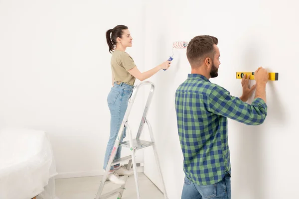 コンテンツ若いです女性Stpladderと絵画壁に立っている間に彼女のボーイフレンドは レベルを使用して線を描く — ストック写真