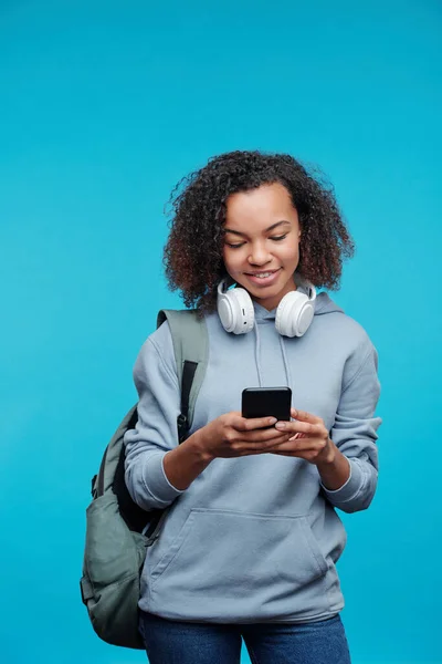 用蓝色背景的电话发短信向现代非洲裔美国高中女生微笑 — 图库照片