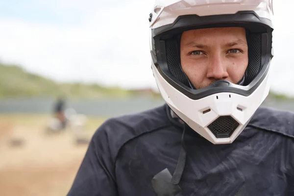 オフロードトラックで白いヘルメットに深刻な若い男性のオートバイの肖像画 — ストック写真
