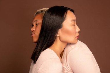 Genç Asyalı ve Afro-Amerikalı kadınlar gözleri kapalı birbirlerine sarılıyorlar ve başlarını omuzlarında tutuyorlar.