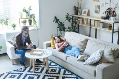 Depresyondaki genç kadın kanepeye uzanıp sorunlarını psikologla paylaşıyor.