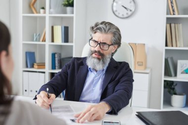 Gözlüklü, ciddi, olgun bir adamın insan kaynakları müdürü olarak çalıştığı ve tanınmayan bir kadınla röportaj yaptığı bir fotoğraf.