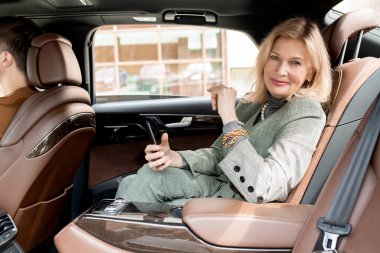 Başarılı bir iş kadını akıllı telefon kullanıyor ve buluşmaya giderken taksinin arka koltuğunda otururken gülümseyerek sana bakıyor.