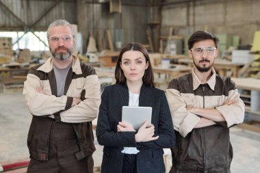 Üniformalı ve koruyucu gözlüklü genç işçiler yeni mobilya taslağını gösterip meslektaşlarına dışlıyorlar.