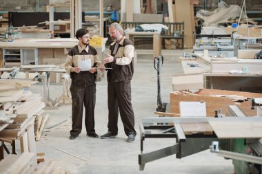 Modern fabrikanın genç işçisi atölye boyunca ilerlerken büyük bir kutu dolusu atölye artıklarıyla el arabası itiyor.