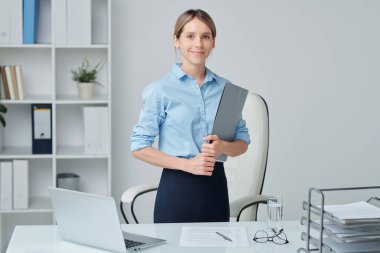 Masa ve koltuk arasında duran genç başarılı sekreter ya da resmi giyim şirketinin başkanı mali belge tutuyor.