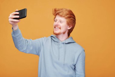 Turuncu arka planda yeni bir ürün sunarken el kol hareketi yapan gülümseyen kızıl saçlı adamın portresi.