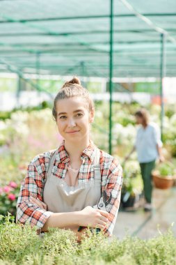 İş kıyafetlerinde başarılı bir bahçıvan. Elinde pense, kollarını göğsünde çapraz bağlayarak yeşil bitkilerle büyük bir çiçek tarlasında duruyor.