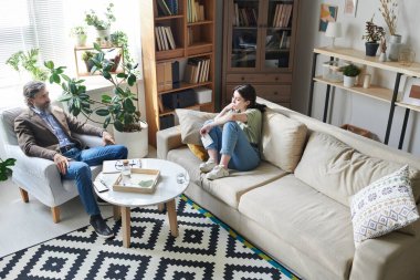 Profesyonel psikoloğun terapi seansında depresyondaki genç kadını dinlerken yüksek açılı görüntüsü.