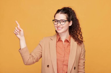 Kolsuz gömlek giyen kıvırcık saçlı kızın portresi turuncu arka plana haplar döküyor.