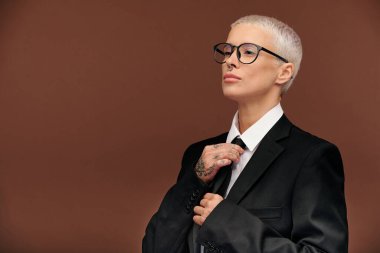 Genç, zarif, erkek, kısa sarı saçlı, iş için giyinirken siyah kravat takan ya da münferit bir etkinlikte resmi giyinen bir kadın.