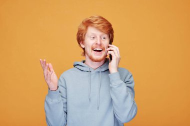 Turuncu arka planda yeni bir ürün sunarken el kol hareketi yapan gülümseyen kızıl saçlı adamın portresi.