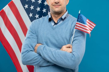 Orta yaşlı bir avukat ya da işadamı göğsünde çapraz kollar ve kameranın önünde dururken küçük bir bayrak tutuyor.