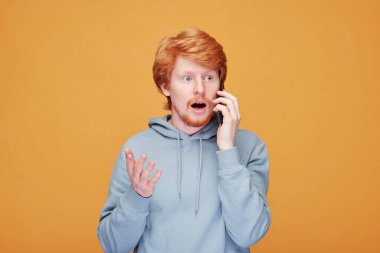 Kapüşonlu, turuncu arka planda gülümseyen kızıl saçlı, yaratıcı bilişim yöneticisi portresi