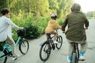 Aktif bir aile olan karı koca ve ilkokul çağındaki oğulları güneşli bir günde ya da sabah saatlerinde modern parkta bisiklet sürüyorlar.