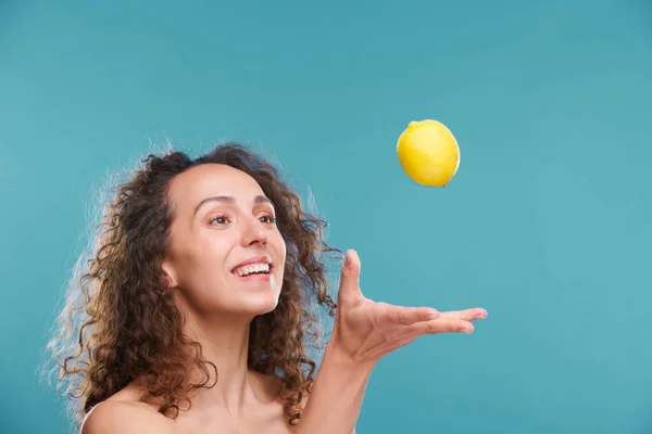年轻快乐的女人 面带微笑 一头乌黑的波浪般的长发 把新鲜柠檬扔在镜头前 孤零零地看着它 — 图库照片