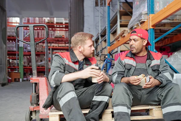 Two Young Intercultural Workers Sitting Industrial Cart Warehouse Environment Discussing — Stock Photo, Image