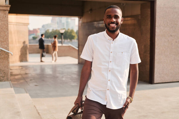 Портрет веселого красивого молодого черного менеджера в белой рубашке, идущего на встречу с клиентом