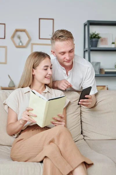 身穿白衬衫的年轻人一边在网上商店冲浪 一边给他的妻子看新书 给他的妻子看智能手机中新型家用电器的照片 — 图库照片