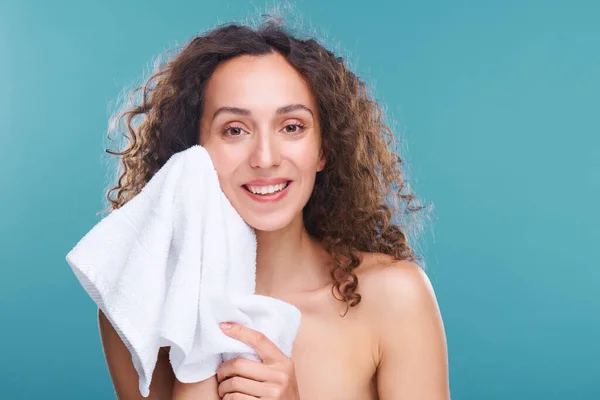 明るく健康な女性とともに歯の笑顔と茶色の波状毛で彼女の顔に触れます柔らかい白いタオルで後の朝の衛生で隔離 — ストック写真