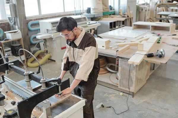 Çağdaş fabrika kıdemli işçisi, atölyenin iç kısımlarına karşı ahşap işlemek için endüstriyel makinenin önünde eğilirken sana bakıyor.