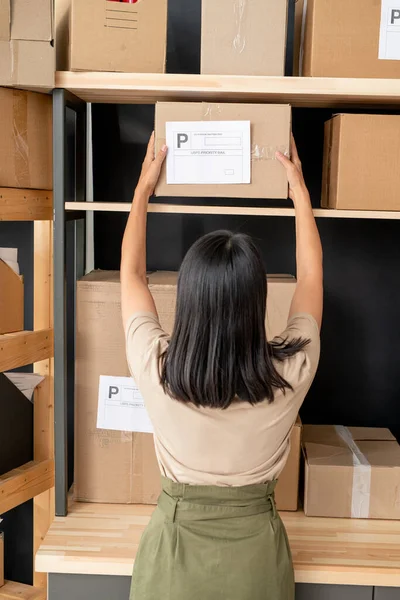 Koyu renk uzun saçlı genç bayan yöneticinin ahşap raftan müşterilerinin siparişleriyle dolu karton kutuları alıp...