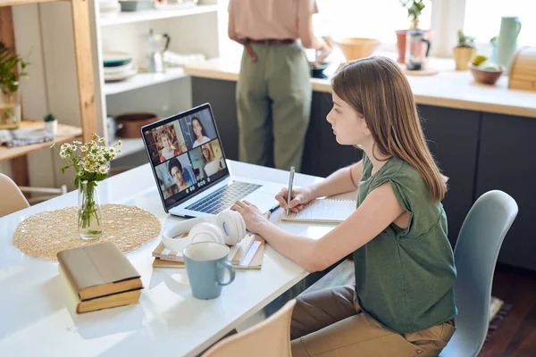 Çevrimiçi iletişim platformu dersi sırasında dizüstü bilgisayarda öğretmenine ve birkaç sınıf arkadaşına bakan sevimli liseli kız.