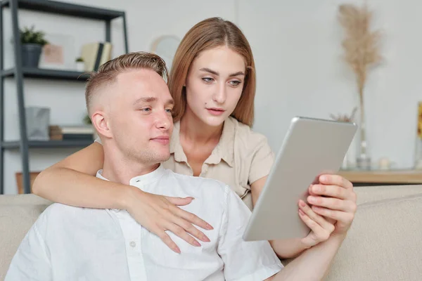 Jovem Afetuosa Com Tablet Abraçando Seu Marido Mostrando Lhe Roupas — Fotografia de Stock