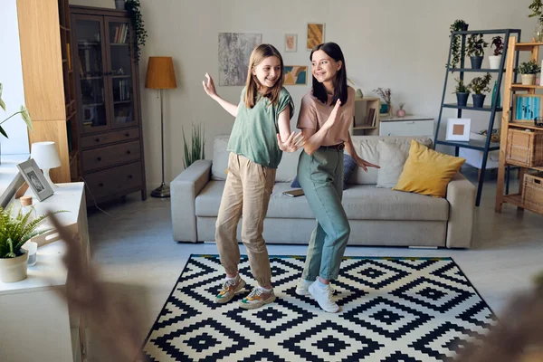 Genç, neşeli esmer kadın ve onun tatlı genç kızı oturma odasında siyah beyaz halıda dans ediyorlar.