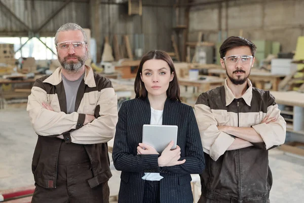 Üniformalı ve koruyucu gözlüklü genç işçiler yeni mobilya taslağını gösterip meslektaşlarına dışlıyorlar.