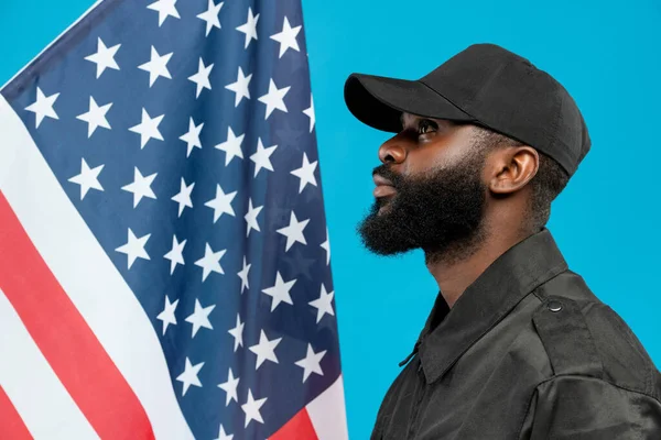 身穿黑色制服 头戴黑色帽子 留着胡子的年轻非洲裔美国男性 面对着星条旗站在摄像机前 — 图库照片