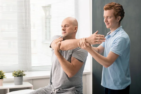 Jonge Hedendaagse Fysiotherapeut Stand Volwassen Mannelijke Patiënt Houd Hem Door — Stockfoto