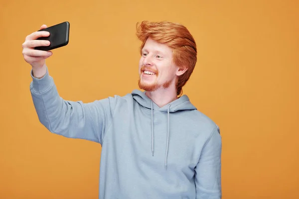 在橙色背景下推出新产品时 笑容可亲的红头发男人站在一边的肖像 — 图库照片