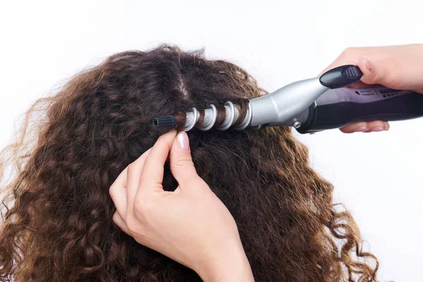 Genç esmer bayanın kafasının arkasında uzun siyah saçları, beyaz arka planda kuaför tarafından elektrikli aletle kıvrılmış.