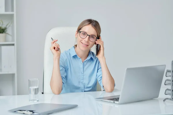 Successful and confident head of business company sitting by desk in office and consulting clients on the phone in front of camera