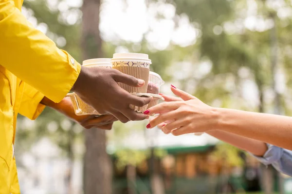 Руки Курьера Мужчины Жёлтой Форме Передают Парке Два Стакана Кофе — стоковое фото