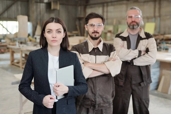 Üniformalı ve koruyucu gözlüklü genç işçiler yeni mobilya taslağını gösterip meslektaşlarına dışlıyorlar.