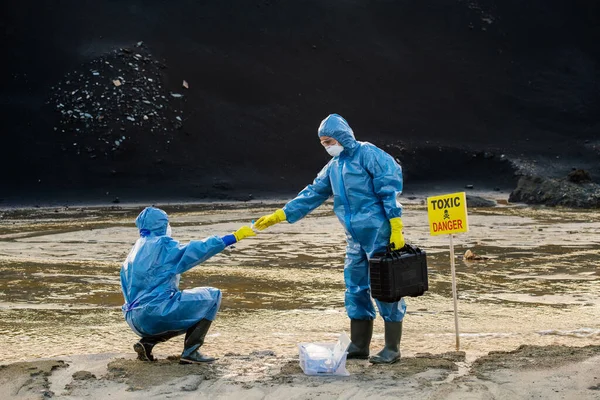 Tehlikeli bölgelerde araştırma yaparken, meslektaşının elindeki kirlenmiş su ya da toprak numunesiyle matarayı alan genç bir kadın çevreci.