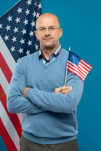 Orta yaşlı, kendine güvenen bir avukat ya da işadamı göğsüne silah dayayıp kameranın önünde dururken küçük bir bayrak tutuyor.