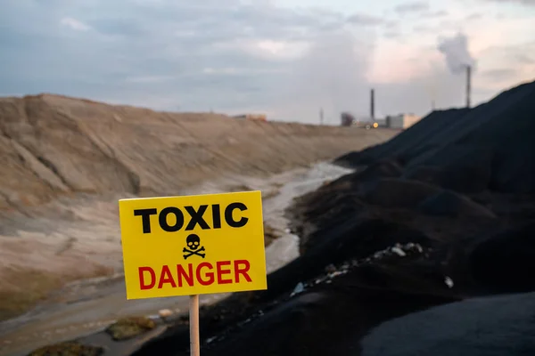 汚れた川 丘や産業用パイプに対するカメラの前で毒性と危険な領域について発表スティック上の長方形の黄色のボード — ストック写真