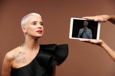 İnsan elleri ekranında zarif bir kadının olduğu tableti tutuyor. Sarışın transseksüel bir kadının önünde. Göğsünde siyah bir tişört takıyor.