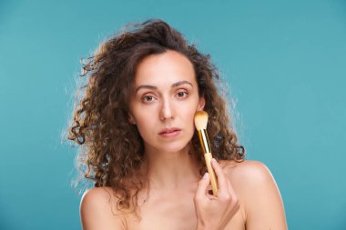 Genç, güzel bir kadın yüzüne makyaj yaparken toz veya allık için makyaj fırçasıyla dokunuyor.