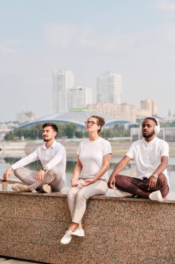 Sakin genç çoklu etnik arkadaşlar zihin odaklı Şehir nehrine karşı oturan ve birlikte meditasyon