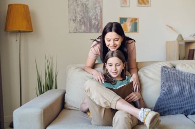 Güzel, genç, gülümseyen bir kadın. Çenesi zeki, genç bir kızın kafasında. Açık kitap okuyup evde otururken.