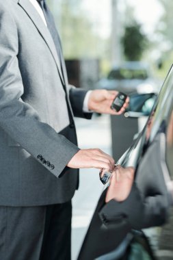 Otomobillerden birinin yanında durup kapıyı açarken uzaktan kumandalı alarm sistemi kullanan şık, genç bir araba satıcısı.