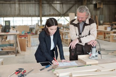 Dokunmatik yastıklı genç bir yönetici ve iki üniformalı erkek işçi atölyenin iç kısımlarına karşı sırada beklerken kollarını göğsünde kavuşturuyorlar.