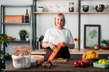 Olgun ev hanımı mutfak masasında taze yeşil armut keserken aynı zamanda ev ortamında kış için çeşitli meyveler hazırlıyor.
